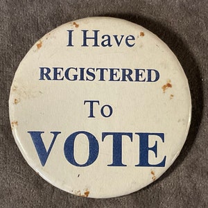 May include: A round, off-white button with the text "I Have REGISTERED To VOTE" in blue. The button has some brown spots and is slightly worn. A political statement.