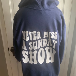 May include: A navy blue hooded sweatshirt with the text "NEVER MISS A SUNDAY SHOW" printed in white on the back.