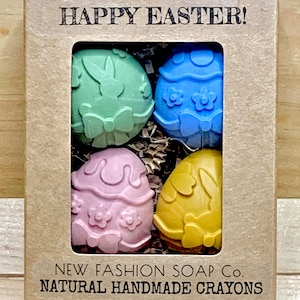 May include: A box of four natural handmade crayons shaped like Easter eggs. The crayons are green, blue, pink, and yellow. The box is brown and has the text "HAPPY EASTER!" and "NEW FASHION SOAP CO. NATURAL HANDMADE CRAYONS" printed on it.