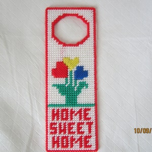 May include: A red, white, and green door hanger with a flower design and the text "HOME SWEET HOME".