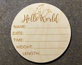 Puede incluir: Una placa redonda de madera con el texto "Hello World" y espacios para rellenar el nombre, la fecha, la hora, el peso y la longitud del bebé. La placa está decorada con una ilustración de un zorro.