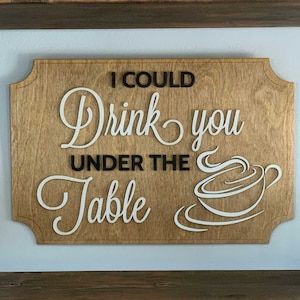 May include: Wooden sign with the text "I could drink you under the table" in black lettering and a white coffee cup illustration.
