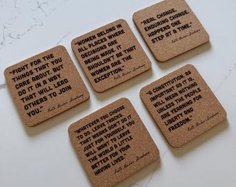 Puede incluir: Juego de cinco posavasos cuadrados de corcho con citas inspiradoras en texto negro. Las citas incluyen: "Lucha por las cosas que te importan" y "El cambio real ocurre paso a paso".
