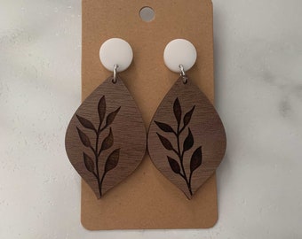 Puede incluir: Un par de pendientes de madera marrón con un diseño de hoja blanca. Los pendientes tienen forma de lágrima y tienen una parte superior redonda blanca.