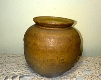 May include: A round, brown ceramic jar with a wide opening and a slightly raised rim. The jar has a smooth, textured surface and a warm, earthy tone. The jar is likely used for storage or decoration.