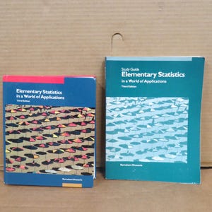May include: Two books titled "Elementary Statistics in a World of Applications" are shown. The book on the left has a blue cover with a colourful pattern, while the one on the right is a study guide with a teal cover.