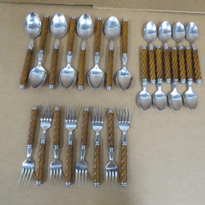 Puede incluir: Un conjunto de cucharas y tenedores de acero inoxidable con mangos trenzados marrones. La cubertería está dispuesta en filas, mostrando el diseño y la cantidad de cada utensilio. Adecuado para una cena formal.