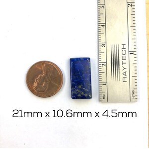 May include: A dark blue lapis lazuli gemstone cabochon, measuring 21mm x 10.6mm x 4.5mm. The gemstone is rectangular in shape and has a speckled pattern.