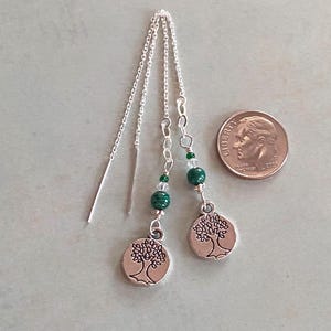 May include: A pair of silver earrings with a tree of life charm, green malachite beads, and clear crystal beads. The earrings are hanging from a silver chain.