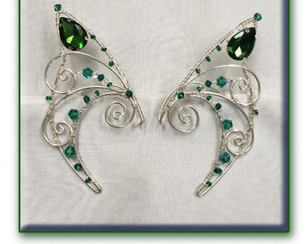 May include: A pair of silver wire elf ears with green crystal accents. The ears are designed to be worn on the upper part of the ear.