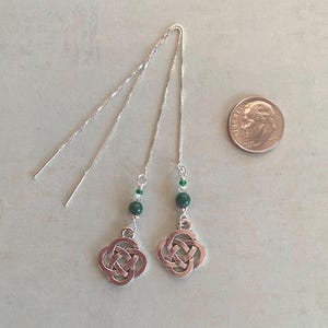 May include: A pair of silver Celtic knot earrings with green beads and silver chains. The earrings are about the size of a US dime.