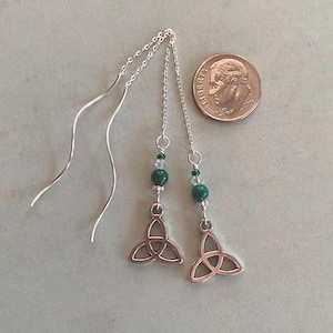 May include: Silver dangle earrings with a green stone and a silver Celtic knot charm. The earrings are about the size of a dime.