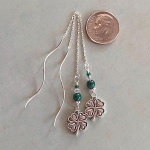 May include: A pair of silver dangle earrings with green malachite beads, clear crystal beads, and silver four-leaf clover charms.