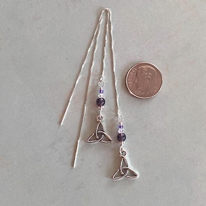 May include: A pair of silver earrings with a Celtic knot design and purple beads. The earrings are hanging from a silver chain.
