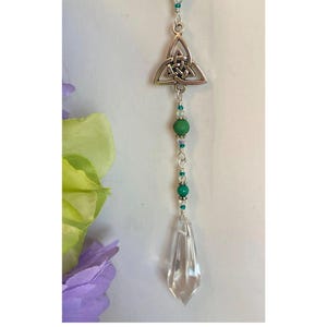 May include: A crystal suncatcher with a silver Celtic knot charm and green beads hanging from it.