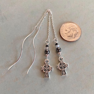 May include: Silver dangle earrings with a Celtic cross charm and black beads. The earrings are approximately the size of a US dime.