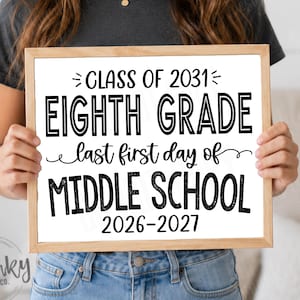 May include: A square wooden sign with a white background and black text that reads: CLASS OF 2031, EIGHTH GRADE, last first day of, MIDDLE SCHOOL, 2026-2027. The sign features a simple light wood frame and is held up by a person in a dark shirt.