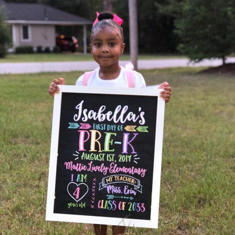May include: A young girl holding a chalkboard sign with the words "Isabella's First Day of Pre-K." The sign also includes the date, school name, teacher's name, and the text "4 years old, Class of 2033."