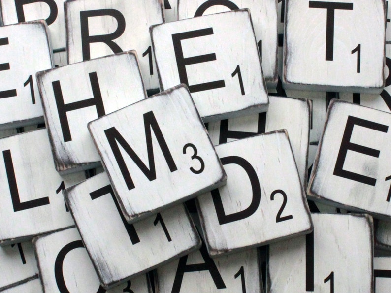 May include: White wooden tiles with black letters spelling out the word "REMTED" with the letter "M" having a value of 3. The tiles are worn and have a distressed look.