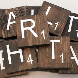 May include: A set of wooden Scrabble tiles with white letters and numbers. The tiles are arranged in a pile, with the letters "A", "R", "T", "H", and "T" visible.