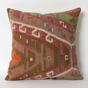 May include: A decorative pillow with a geometric pattern in shades of brown, pink, and orange. The pillow is made of woven fabric and has a fringed edge.