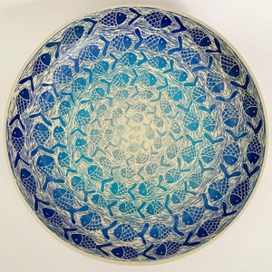 Op de afbeelding: Een witte keramische kom met een blauw en wit ontwerp van gestileerde vissen. De vissen zijn in een cirkelvormig patroon gerangschikt, waardoor een spiraaleffect ontstaat. De kom is perfect om snacks of salades in te serveren.