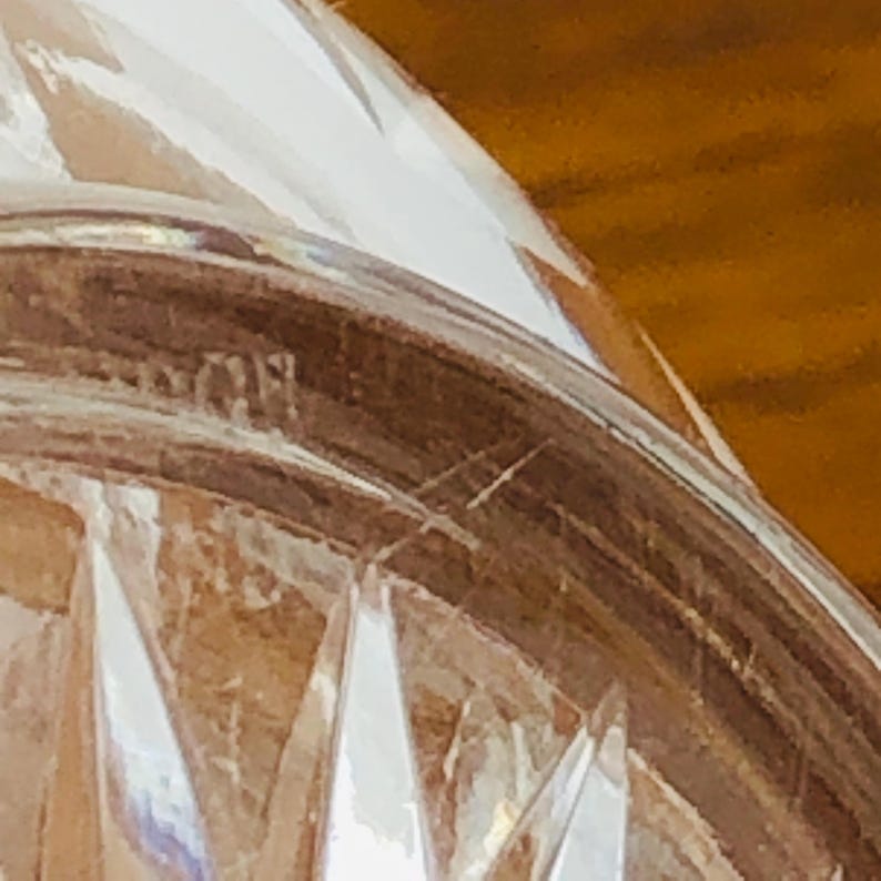 May include: Close-up of a clear, faceted glass object. The glass has a diamond-cut pattern and a curved shape. The object appears to be a decorative piece, possibly a bowl or a vase. The background is a warm, wooden surface.