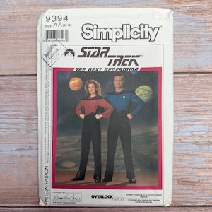 Peut inclure: Une pochette de patron de couture Simplicity, numéro 9394, taille AA (6-16), présentant des modèles d'uniformes Star Trek: The Next Generation. La couverture montre deux personnes en combinaisons rouge et bleue avec des pantalons noirs.