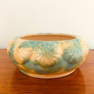 May include: A ceramic planter with a light blue and yellow glaze. The planter is decorated with raised flower designs.