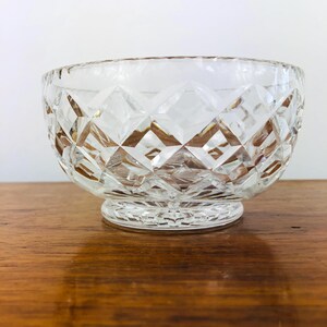 May include: Clear, diamond-cut glass bowl with a round base. The bowl has a wide opening and a textured surface. The bowl is sitting on a wooden surface.