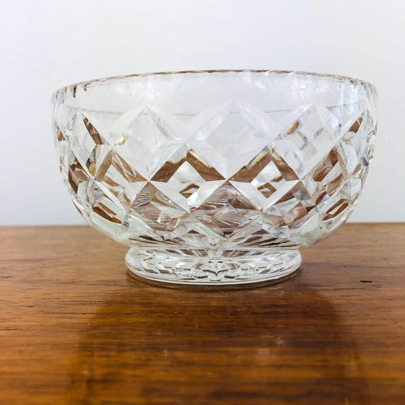 May include: Clear, diamond-cut glass bowl with a round base. The bowl has a wide opening and a textured surface. The bowl is sitting on a wooden surface.