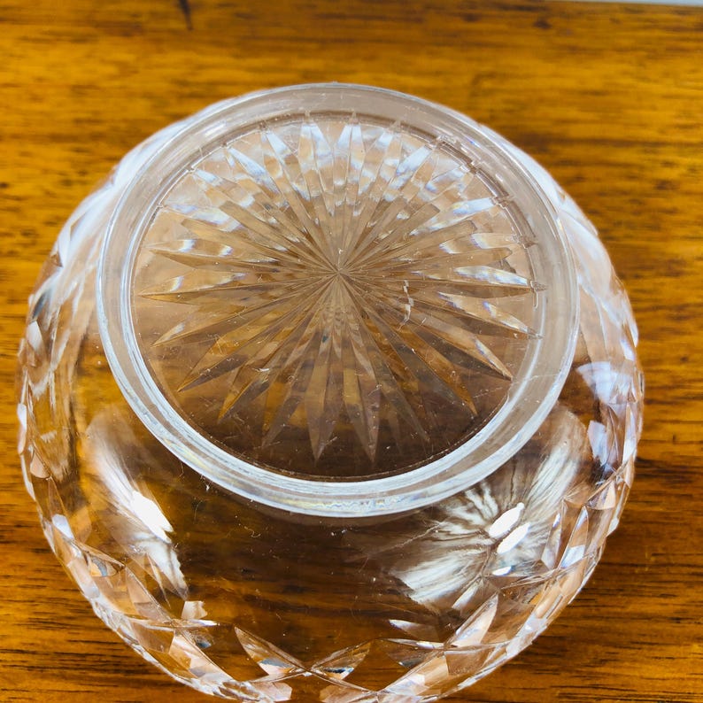 May include: A clear, round crystal bowl with a diamond-cut pattern. The bowl is inverted, revealing the detailed starburst design on the base. The bowl's edges are faceted, reflecting light.