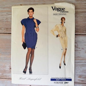 以下が含まれることがあります： Vogue Patternsのソーイングパターン。2つのドレスのデザインが特徴です。半袖と襟付きの青いドレスと、長袖のベージュのドレスが含まれています。パターンには「Karl Lagerfeld」と「Paris Original」と記載されています。