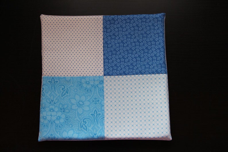 Pu&ograve; includere: Un cuscino quadrato con un design a patchwork. Il cuscino &egrave; realizzato con quattro tessuti diversi, ognuno con un motivo diverso. I tessuti sono rosa con pois bianchi, blu con pois bianchi, blu con un motivo floreale e blu con un piccolo motivo floreale bianco.