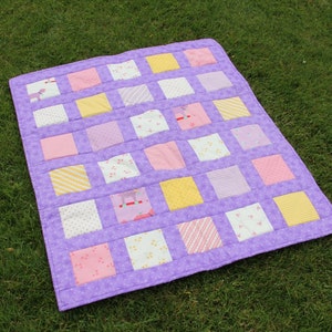 May include: A purple patchwork quilt with squares of different colours and patterns, including pink, yellow and white.