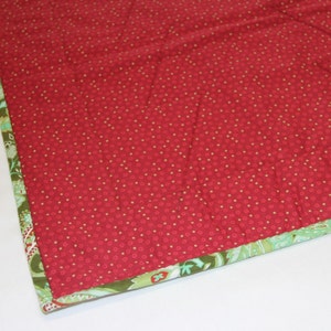 May include: Close-up of a red fabric with a white polka dot pattern. The fabric has a green and white patterned border.