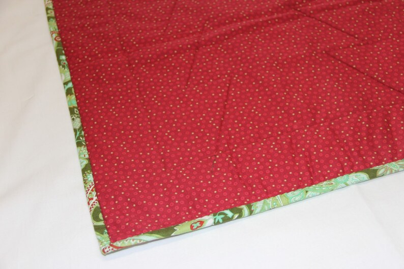 May include: Close-up of a red fabric with a white polka dot pattern. The fabric has a green and white patterned border.