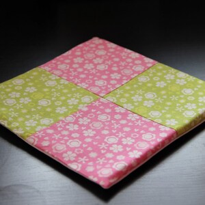May include: A square patchwork cushion with a pink and green floral pattern. The cushion is made of fabric and has a white backing.