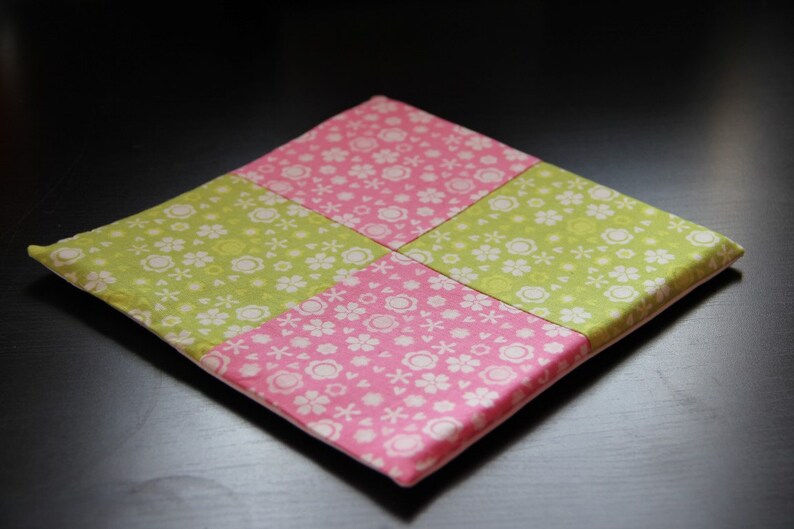 May include: A square patchwork cushion with a pink and green floral pattern. The cushion is made of fabric and has a white backing.