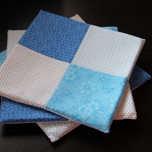 Può includere: Un set di tre quadrati di tessuto blu e bianco con motivi diversi. I quadrati sono cuciti insieme per creare un quadrato più grande.