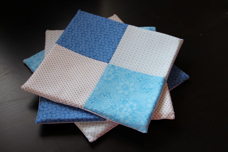 Pu&ograve; includere: Un set di tre quadrati di tessuto blu e bianco con motivi diversi. I quadrati sono cuciti insieme per creare un quadrato pi&ugrave; grande.