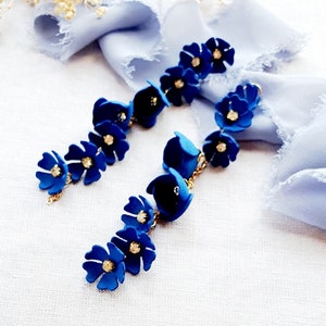 May include: A pair of long, dangling earrings with blue flower charms and gold chain accents. Each earring features five blue flower charms with a rhinestone centre.