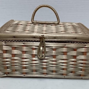 May include: A rectangular woven basket with a handle and a lid. The basket is made of light tan and brown woven material. The handle is arched and made of the same material as the basket. The basket has a clasp closure.