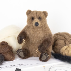 May include: A brown bear needle felting kit with wool, wire, and instructions. The kit includes brown, black, and beige wool, as well as wire for the armature. The kit also includes a needle felting tool and a pair of scissors.