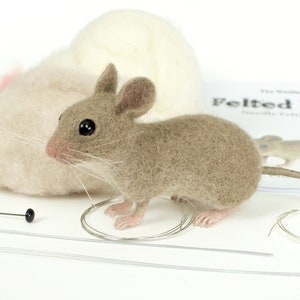 May include: A brown felted mouse with black eyes and a long tail. The mouse is sitting on a white surface with a ball of wool and a needle and thread.