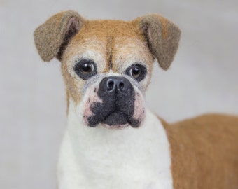 May include: A close-up of a brown and white needle felted dog with black eyes and a black nose. The dog is looking directly at the camera.