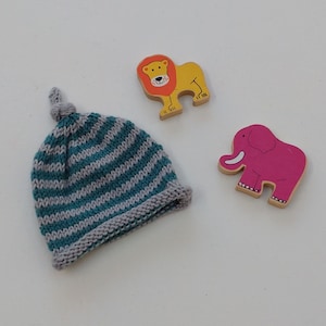 May include: A teal and gray striped knitted baby hat with a knotted top. The hat is next to a wooden toy lion and a wooden toy elephant.