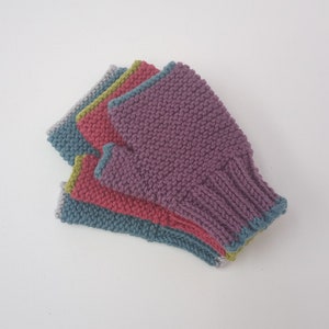 May include: A stack of four knitted fingerless gloves in shades of purple, pink, green, and blue. Each glove has a contrasting trim color. The gloves are made of a textured knit fabric.