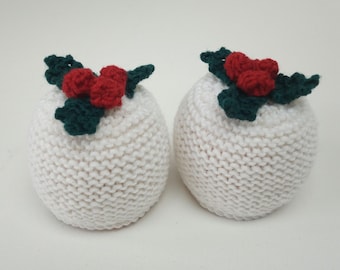 May include: Two white knitted ornaments, each topped with a sprig of green leaves and three red berries. The ornaments have a rounded shape and a textured, knitted surface, perfect for holiday decor.
