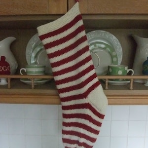 May include: A red and white striped knitted stocking hanging on a wooden shelf. The stocking is made of a soft, cosy yarn and is perfect for holding small gifts.